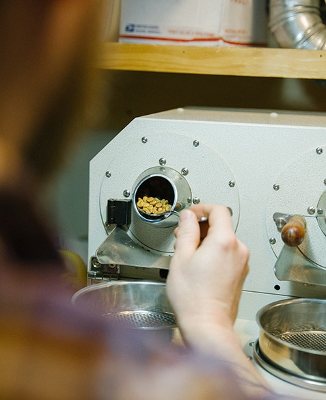 Andrew sample roasts coffee on a double barrel Proaster sample roaster. Using a spoon, he glances at the coffee while it roasts to analyze color, texture, and fragrance.