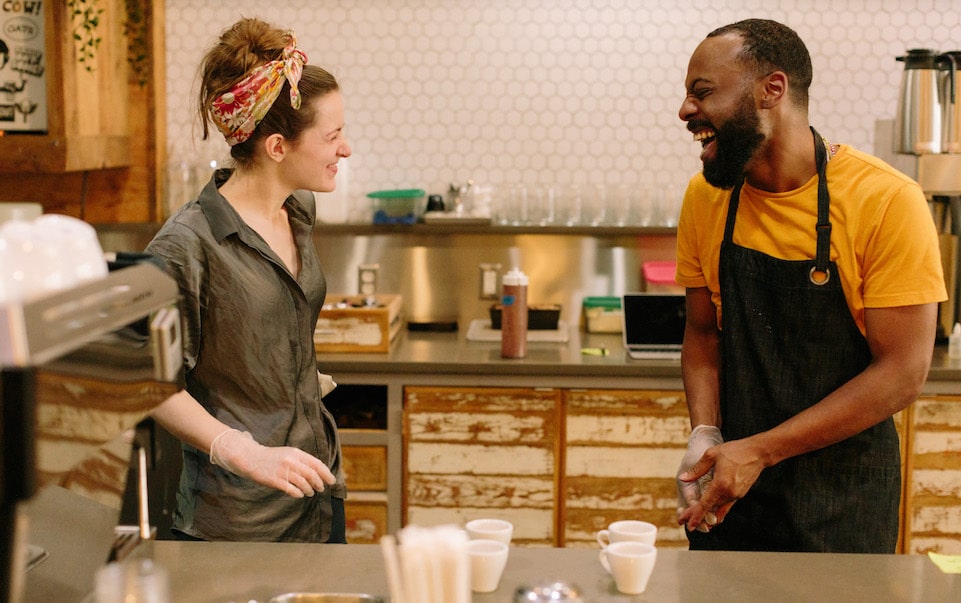 Two members of the Blueprint Coffee Delmar team face each other while laughing